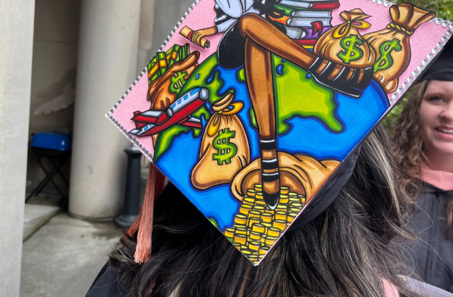 Photo of an MPH student with showing their graduation cap they decorated with motivational quotes