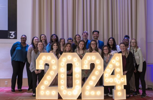 All MPH 2024 graduates standing behind2024 neon sign smiling