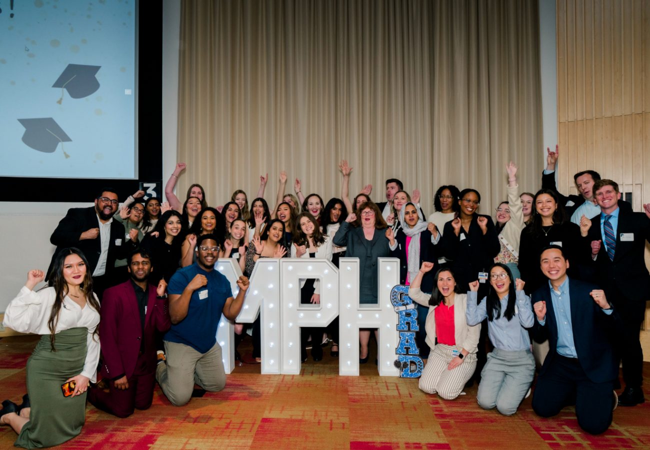 Group of MPH graduates smiling around MPH letter sign with hands in the air smiling