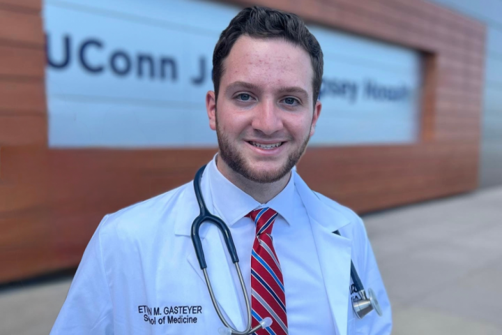 photo of Ethan Gasteyer in his white medical coat in front of UConn's John Dempsey Hospital
